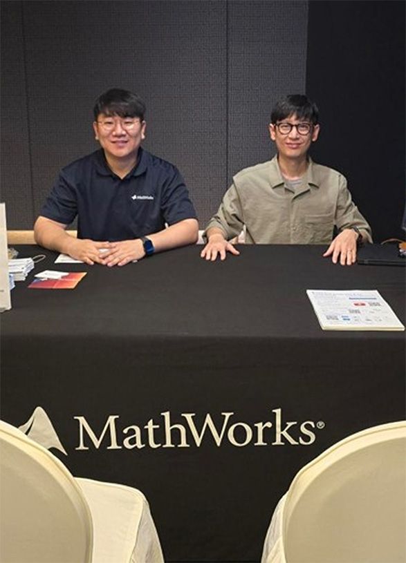 Two people sit at a table with a MathWorks tablecloth and smile at the camera in a conference setting.