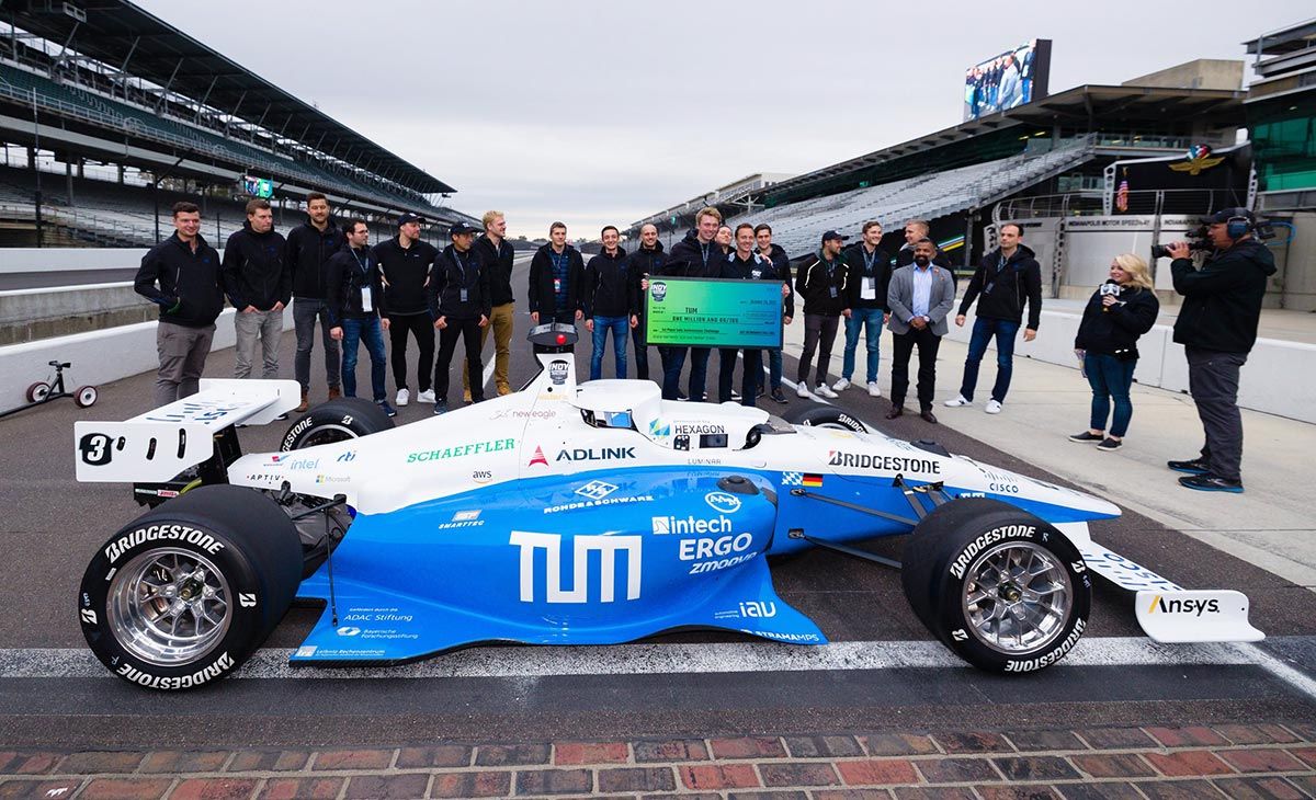 The T U M Autonomous Motorsport team holds the winning 1 million dollar check while standing behind the T U M race car.