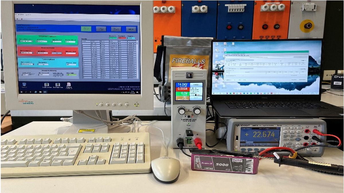 A battery is connected to voltage testing equipment and the results are shown on two computer screens.